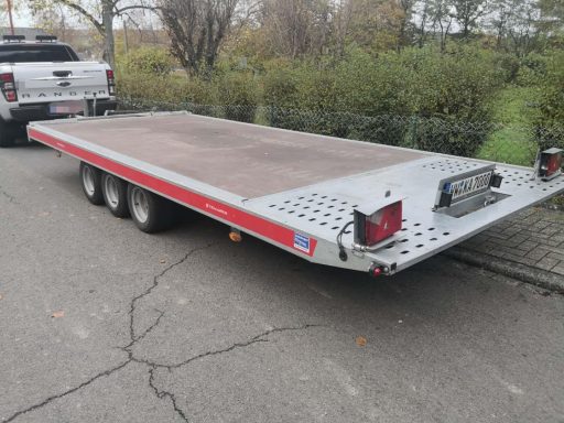 Flacher Anhänger mit drei Achsen, geparkte Lieferung auf Asphaltstraße.