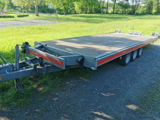 Flacher Anhänger mit einer großen Ladefläche, auf einem grünen Rasenparkplatz.